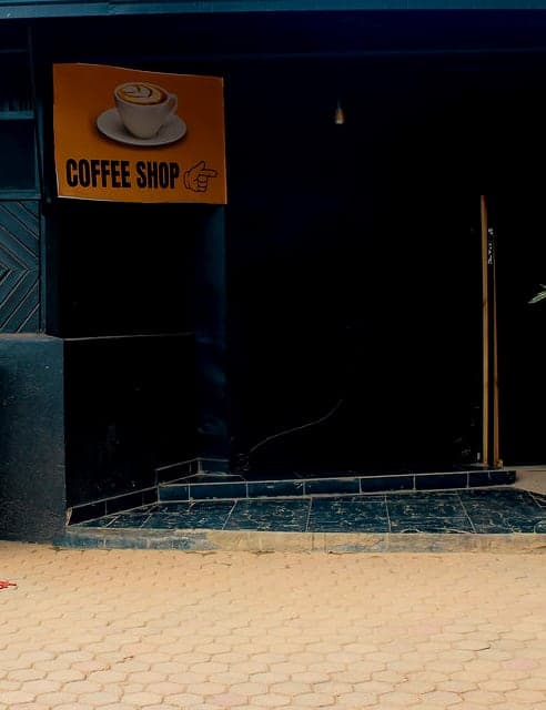 The Coffee Shop sign — a gold panel with a cup of latte — on the black wall beside the entrance