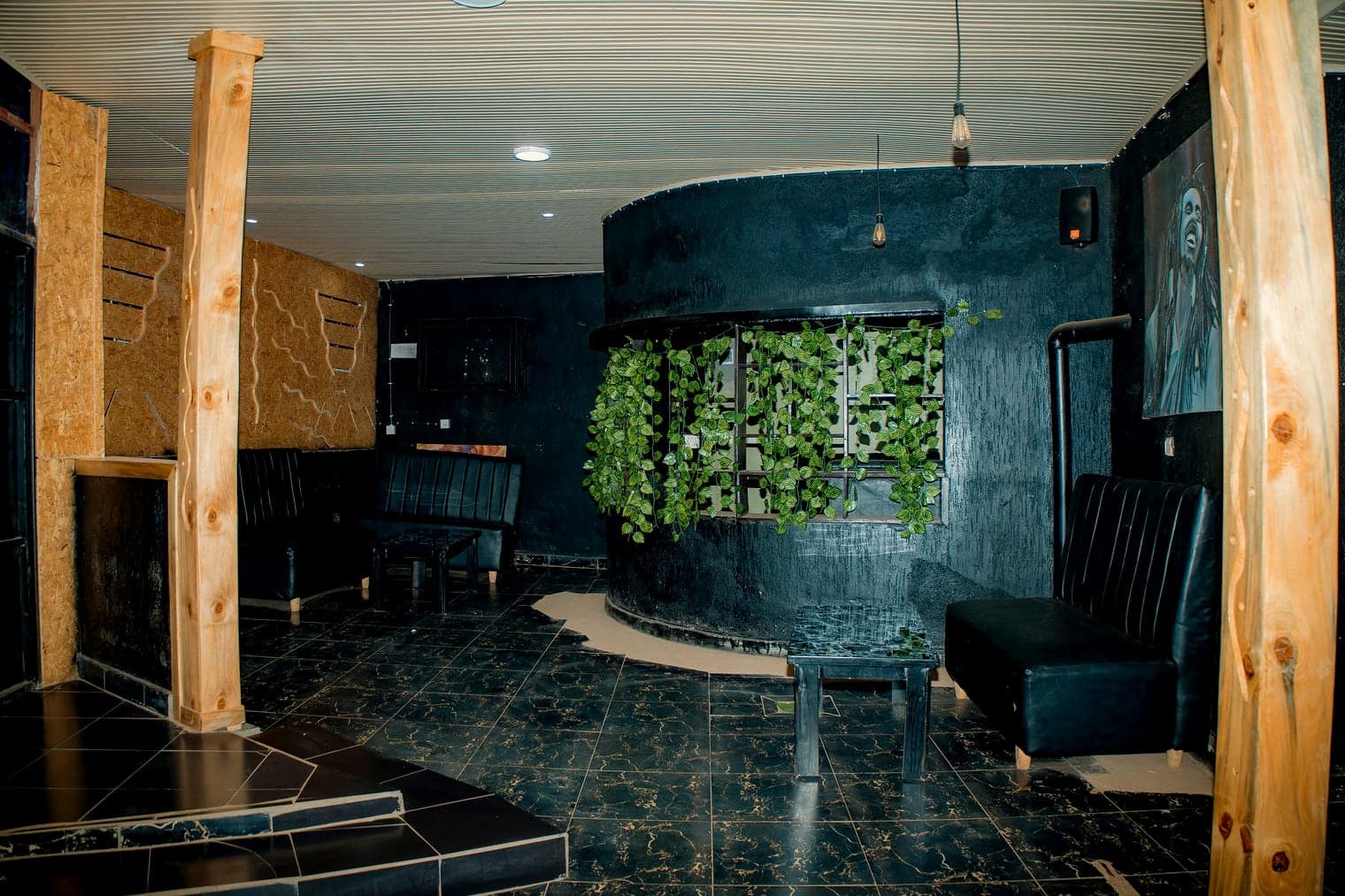 The lounge: raw timber posts, black textured walls, a curved window screened with hanging vines and black leather banquettes